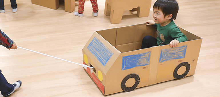 ダンボールでできた車に乗る男の子とそれを引っ張っている子ども