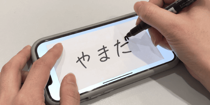 携帯の画面に表示した文字を布に透かしてなぞり書きしている様子